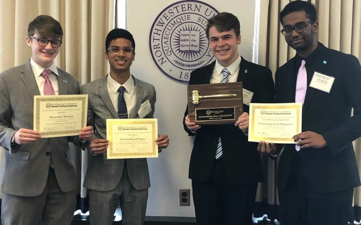 Four students in suits holding the award certificates and gavel plaque they won at a Model United Nations conference
