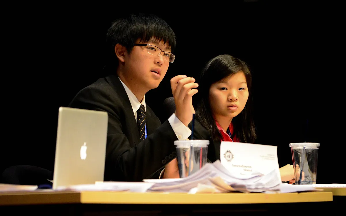 Two student chairs presiding over a Security Council committee at a Model United Nations conference, seated behind a laptop and microphone