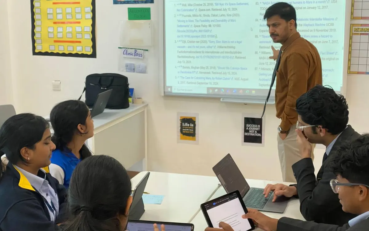 Students with laptops and tablets at a workshop on researching Model UN position papers, a presenter beside a projected slide