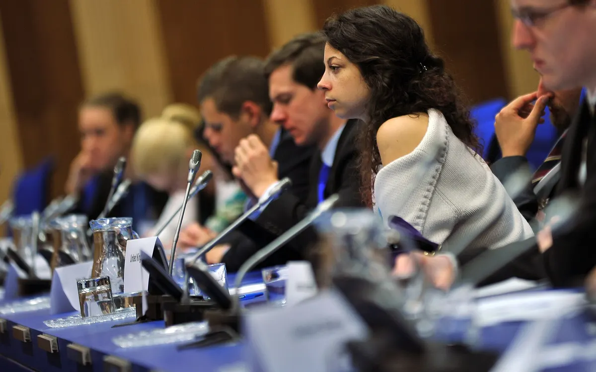 University students debating at the Vienna International Model United Nations, seated behind microphones and country placards