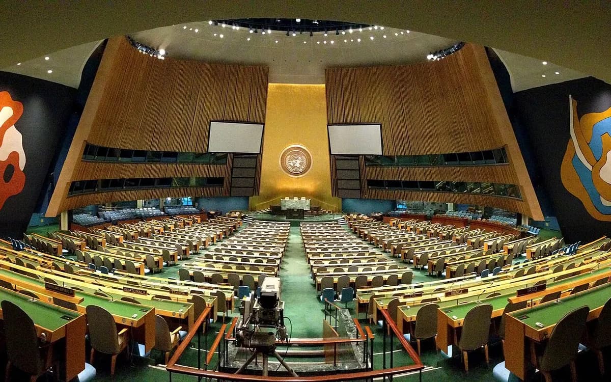 The United Nations General Assembly Hall in New York, seen from the back of the hall, with rows of delegation desks facing the podium and the UN emblem