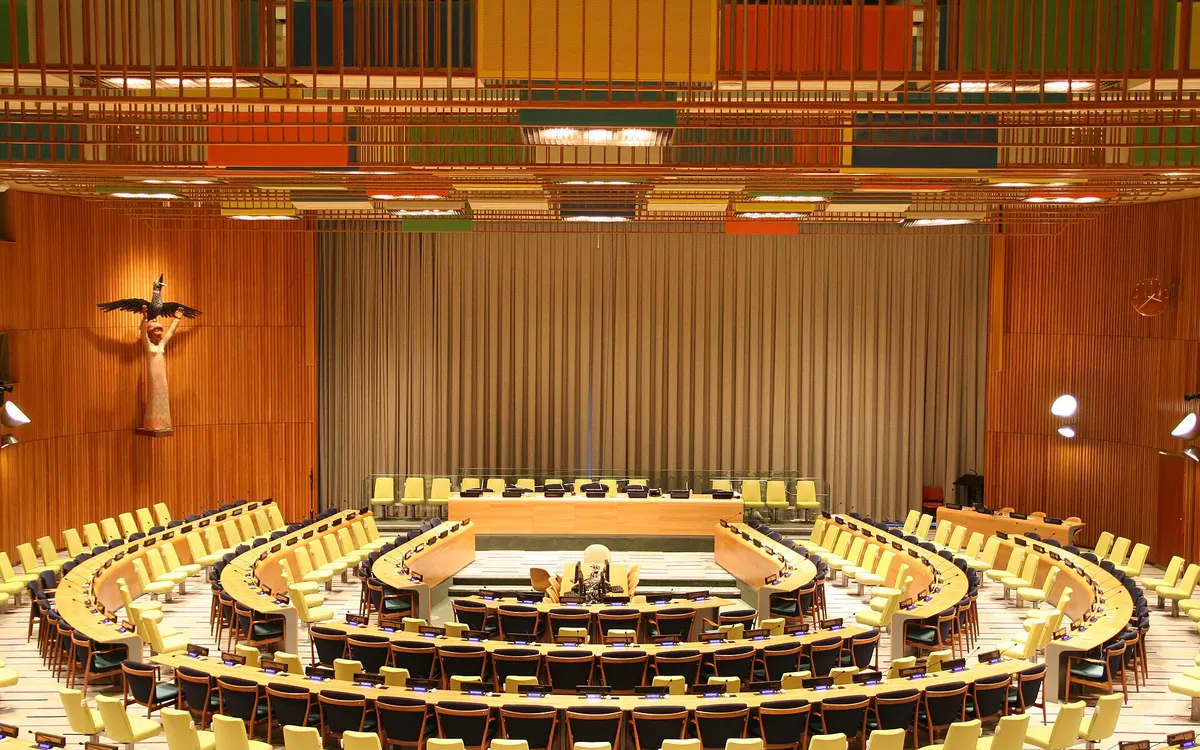 The UN Trusteeship Council chamber in New York: a horseshoe table in the middle of curved rows of seats, with a wooden statue at the end of the room
