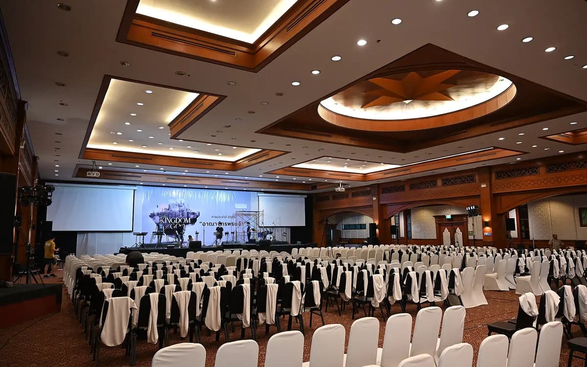 A large hotel conference hall set up with rows of white-covered chairs facing a stage